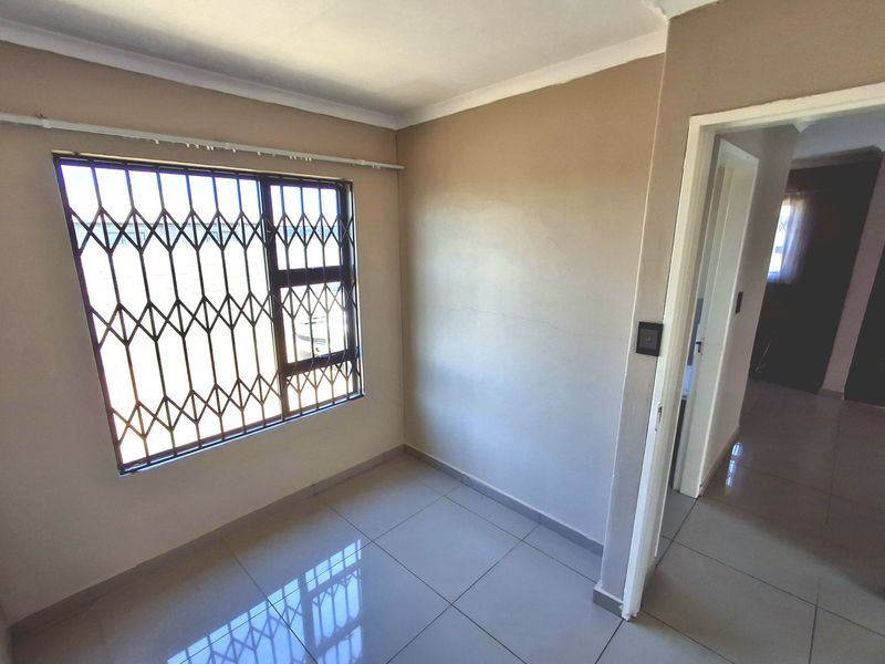 An empty bedroom featuring tiled flooring, neutral walls, and a security gate on the window, providing a blank canvas for personalization.