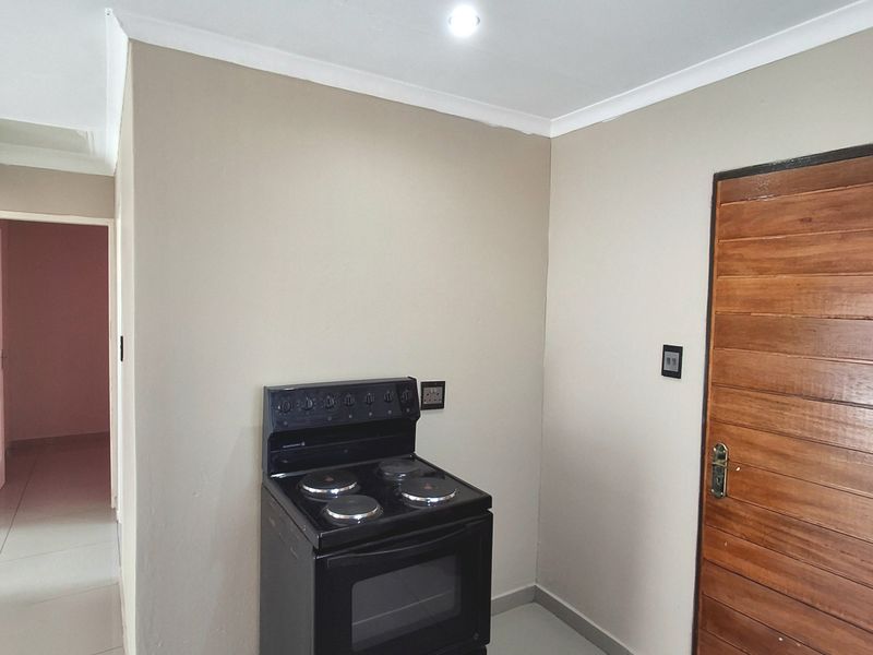 A simple kitchen area featuring tiled flooring, a freestanding electric stove, and a solid wooden door leading to an adjacent space.