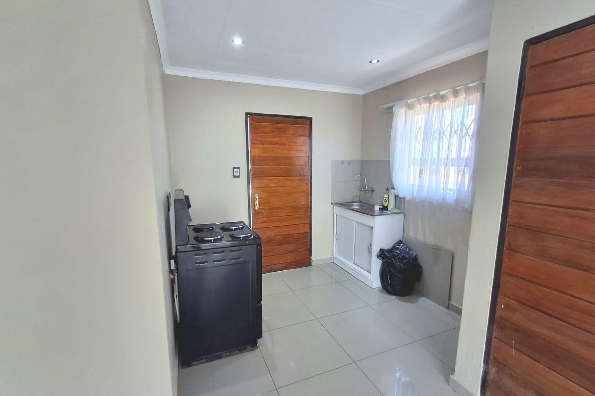 A compact kitchen area featuring tiled flooring, a single sink unit, and a freestanding stove, with neutral wall finishes and wooden door access.