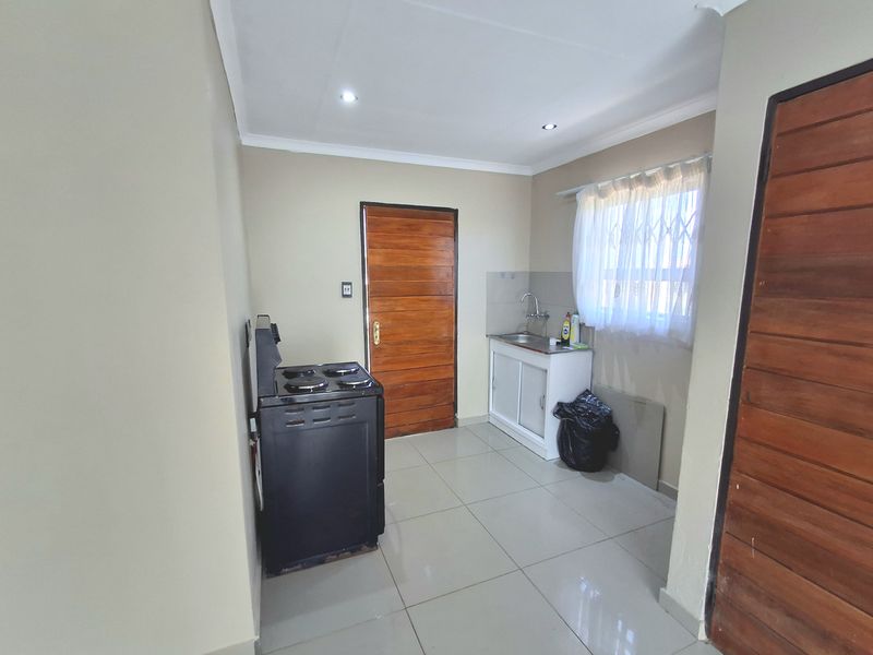 A compact kitchen area featuring tiled flooring, a single sink unit, and a freestanding stove, with neutral wall finishes and wooden door access.