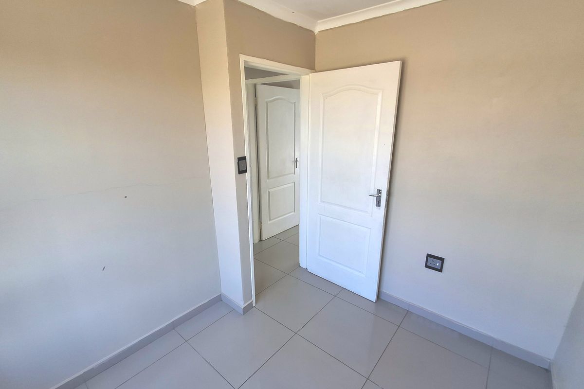 An empty bedroom featuring neutral wall paint, tiled flooring, and panelled interior doors, providing a clean and versatile space ready for furnishing.