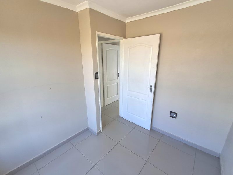 An empty bedroom featuring neutral wall paint, tiled flooring, and panelled interior doors, providing a clean and versatile space ready for furnishing.