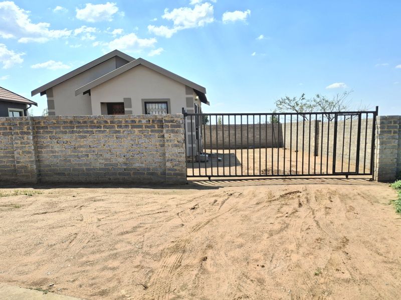 Front view of a residential property featuring a metal sliding gate, perimeter brick walling, and a tiled roof structure.