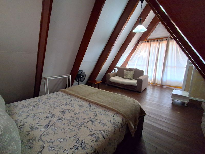 A spacious attic-style bedroom featuring exposed timber rafters, warm timber flooring, and large windows allowing for natural light.