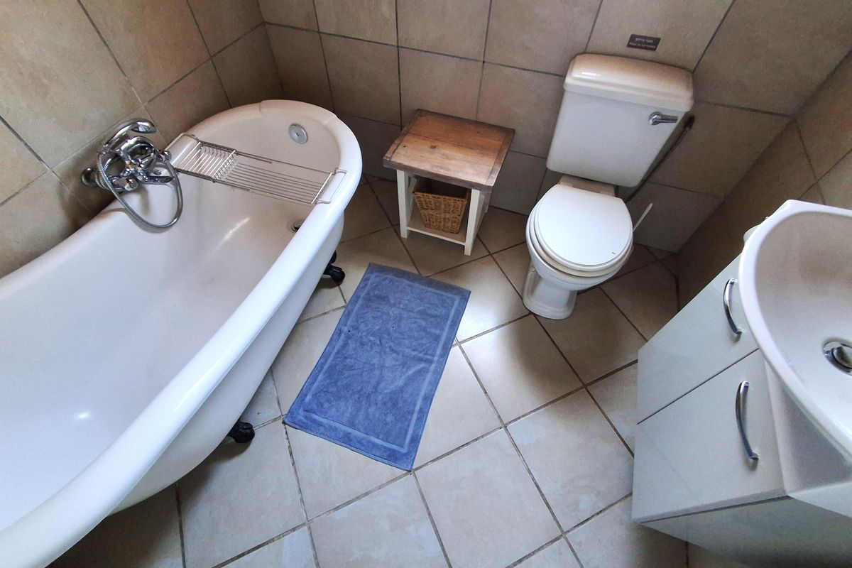 A functional bathroom featuring a classic clawfoot bathtub, a standard toilet, and a vanity cabinet with tiled walls and flooring.