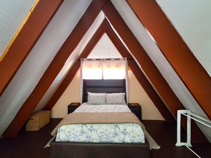 A cozy bedroom located in an A-frame loft space, featuring prominent exposed timber rafters and a pitched ceiling design.