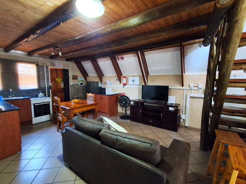 Open plan living and kitchen area featuring exposed timber ceiling beams, tiled flooring, and a timber staircase leading to an upper level.