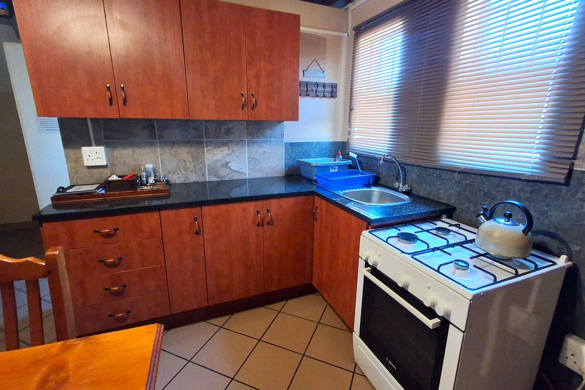 A functional kitchen featuring wood-look cabinetry, granite countertops, a gas stove, and tiled flooring with a neutral backsplash.