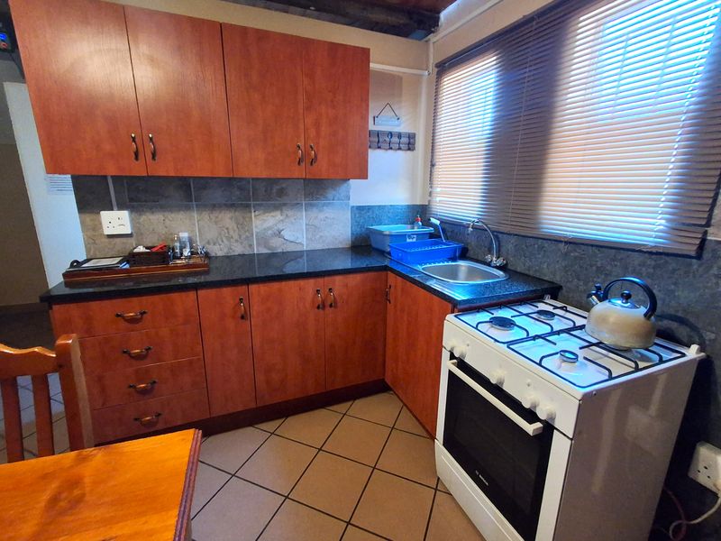 A functional kitchen featuring wood-look cabinetry, granite countertops, a gas stove, and tiled flooring with a neutral backsplash.