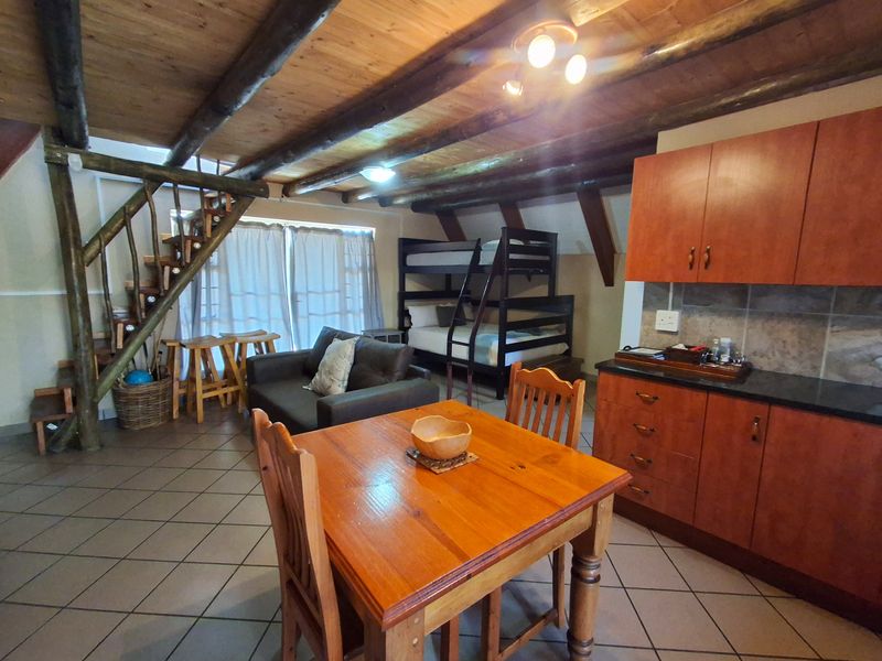 Open-plan living area featuring exposed timber ceiling beams, a wooden staircase, and a compact kitchen with built-in cabinetry and tiled flooring.
