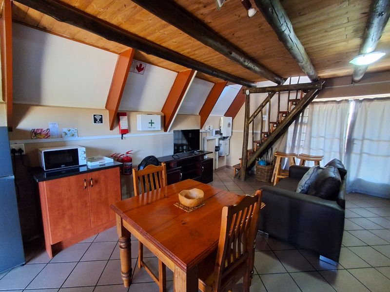 Open-plan living area featuring exposed timber ceiling beams, tiled flooring, and a wooden staircase leading to an upper level.