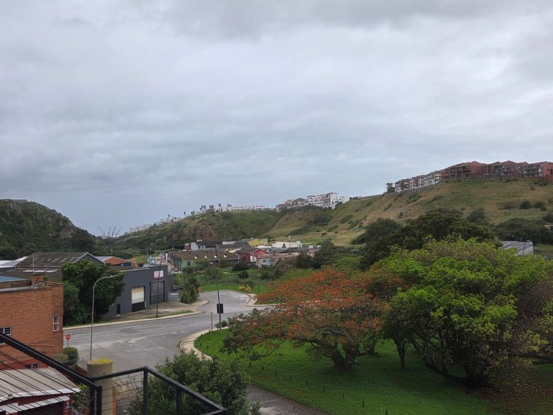 An elevated view overlooking the surrounding neighbourhood, green spaces, and distant hillside residential developments under an overcast sky.