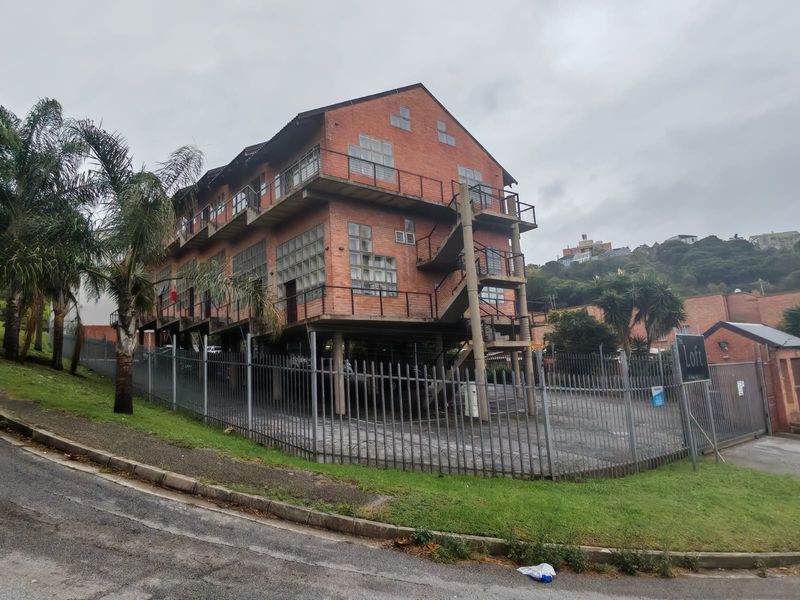 Exterior view of a multi-story apartment building featuring exposed brick architecture, external steel staircases, and secure perimeter fencing.