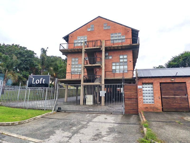 Front view of The Loft apartment building featuring a brick facade, external staircase, balconies, and secure gated access with a private garage.