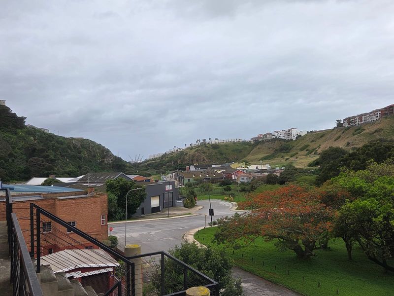 An elevated view overlooking the surrounding neighbourhood, green spaces, and distant hillside residential developments from a balcony with a metal balustrade.