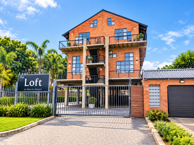 Front elevation of The Loft apartment building featuring a modern brick facade, external stairwell, secure gated entrance, and paved driveway access.