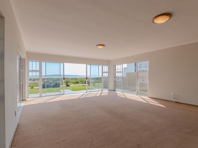 Spacious, light-filled living area featuring expansive sliding glass doors with scenic coastal views and neutral carpeted flooring.