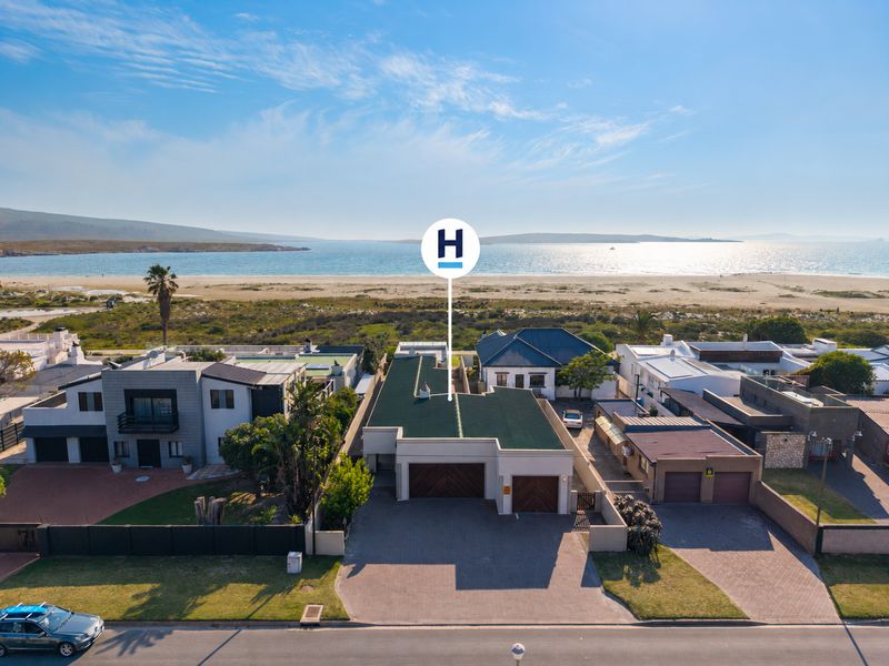 Aerial view of a coastal property featuring a double garage, paved driveway, and direct proximity to the beach and ocean.
