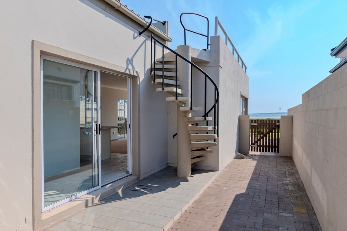 Rear exterior view featuring a paved patio, a spiral staircase leading to a rooftop terrace, and a sliding glass door entrance.