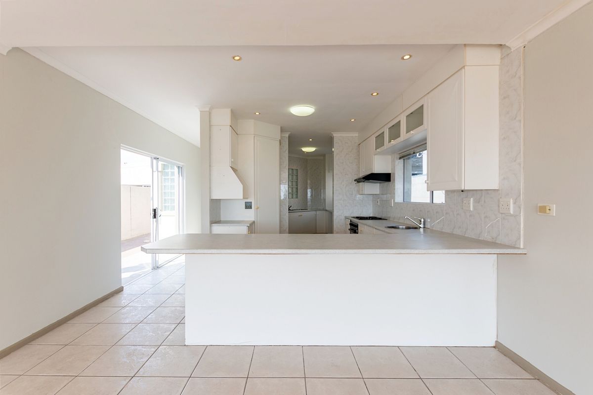 An open-plan kitchen featuring white cabinetry, laminate countertops, built-in appliances, and tiled flooring, with direct access to an outdoor patio area.