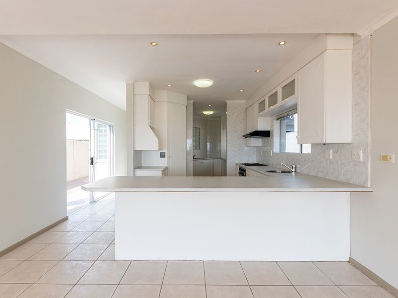 An open-plan kitchen featuring white cabinetry, laminate countertops, built-in appliances, and tiled flooring, with direct access to an outdoor patio area.