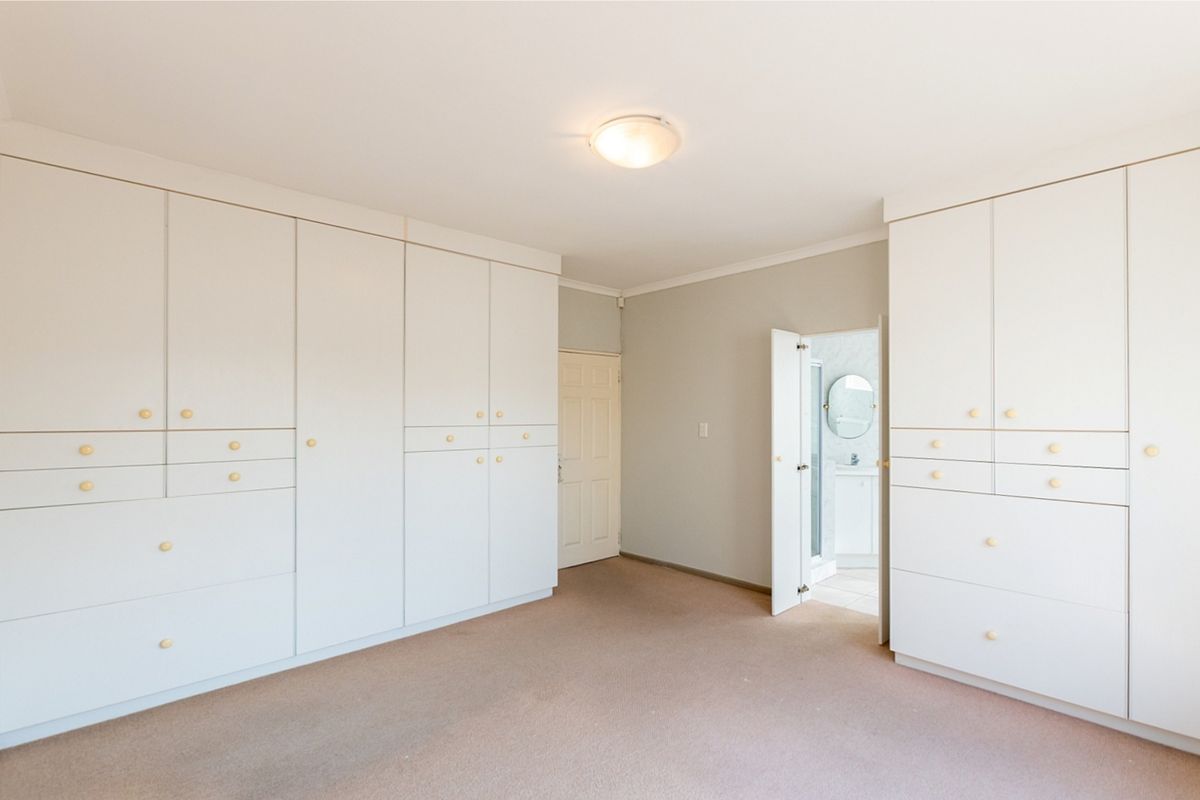 Spacious bedroom featuring extensive built-in white cabinetry, neutral carpeting, and direct access to an en-suite bathroom.