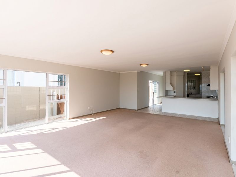 Spacious open-plan living and kitchen area featuring neutral walls, carpeted flooring, and large sliding glass doors providing access to the exterior.