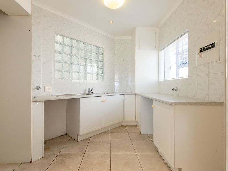 A functional, empty scullery area featuring built-in cabinetry, laminate countertops, a stainless steel sink, and tiled finishes throughout.