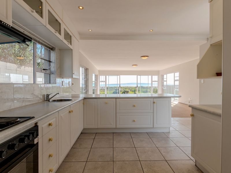 Spacious open-plan kitchen featuring white cabinetry, stone countertops, and integrated appliances, flowing into a bright living area with expansive coastal views.