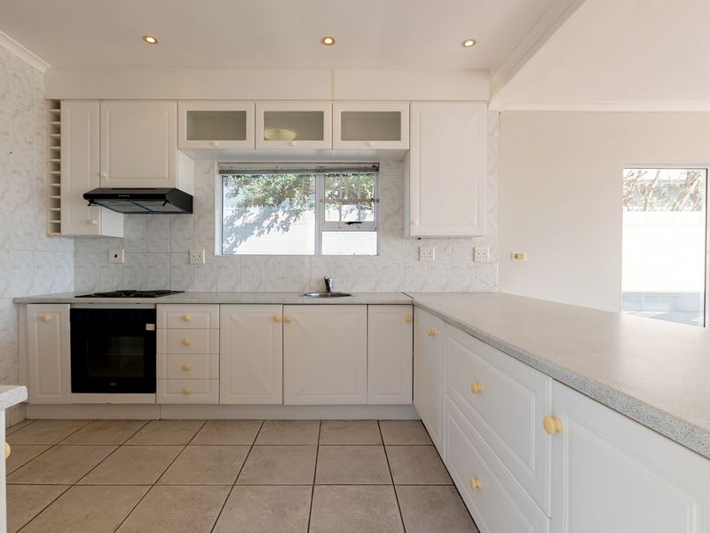 A clean, functional kitchen featuring white cabinetry, laminate countertops, built-in oven, gas hob, and tiled flooring with ample natural light.