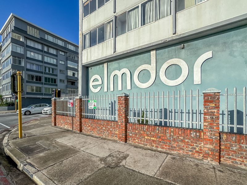 Exterior view of the Elmdor apartment building featuring a brick boundary wall, metal security fencing, and street-level access.