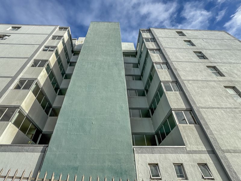 Low-angle view of the apartment building exterior, showcasing the concrete facade, multi-story window layout, and perimeter security spikes.