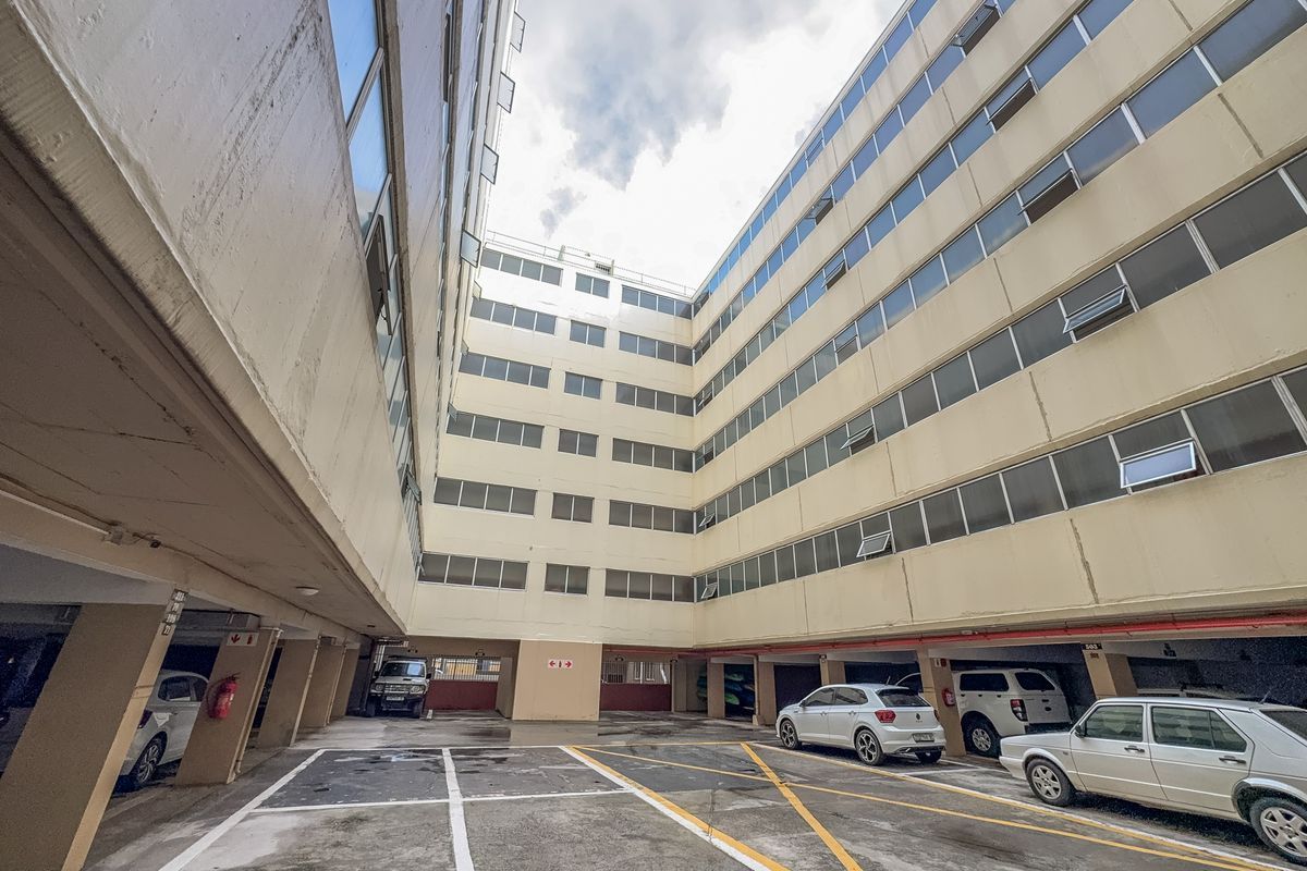 View of the apartment building's rear exterior, featuring a multi-level facade and a paved ground-level parking area.