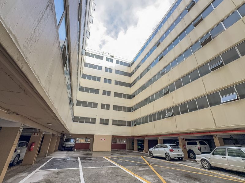 View of the apartment building's rear exterior, featuring a multi-level facade and a paved ground-level parking area.
