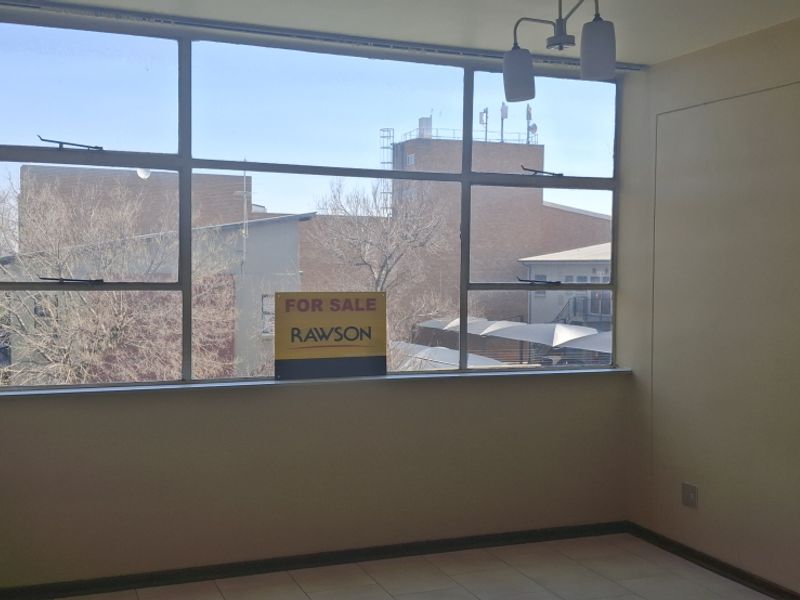 An empty bedroom featuring large metal-framed windows, tiled flooring, and a ceiling light fixture, requiring minor cosmetic updates to the walls.