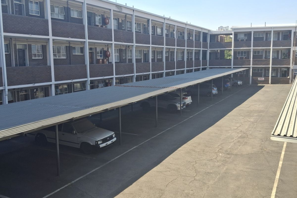 Exterior view of an apartment complex featuring a multi-level brick building with covered parking bays and an asphalt driveway.