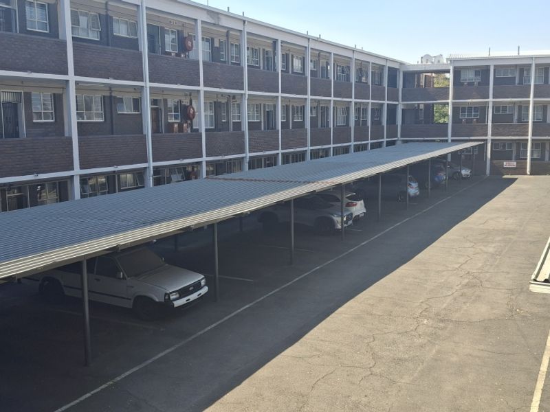 Exterior view of an apartment complex featuring a multi-level brick building with covered parking bays and an asphalt driveway.