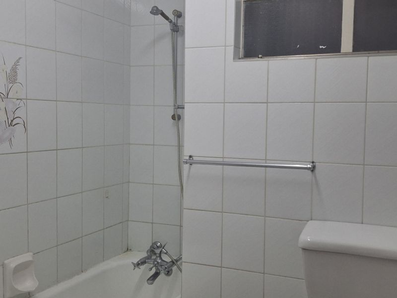 A functional bathroom featuring a bathtub with shower mixer, white wall tiles, and a standard toilet.