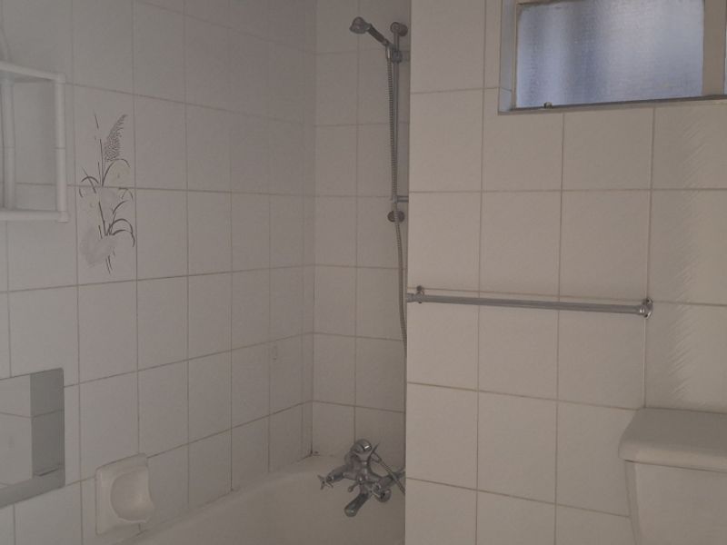 A dated bathroom featuring a bathtub with shower mixer, toilet, and tiled walls, offering potential for a modern renovation.