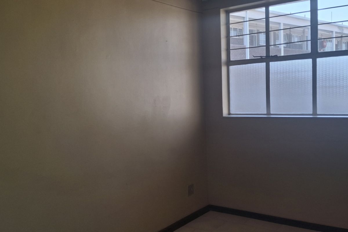 An empty bedroom featuring tiled flooring and a steel-framed window with security bars, requiring minor cosmetic updates to the wall finishes.