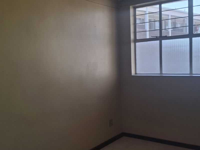 An empty bedroom featuring tiled flooring and a steel-framed window with security bars, requiring minor cosmetic updates to the wall finishes.