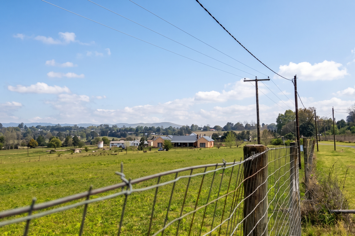 A scenic view of the surrounding rural landscape and open fields, featuring wire fencing and utility infrastructure in the foreground.