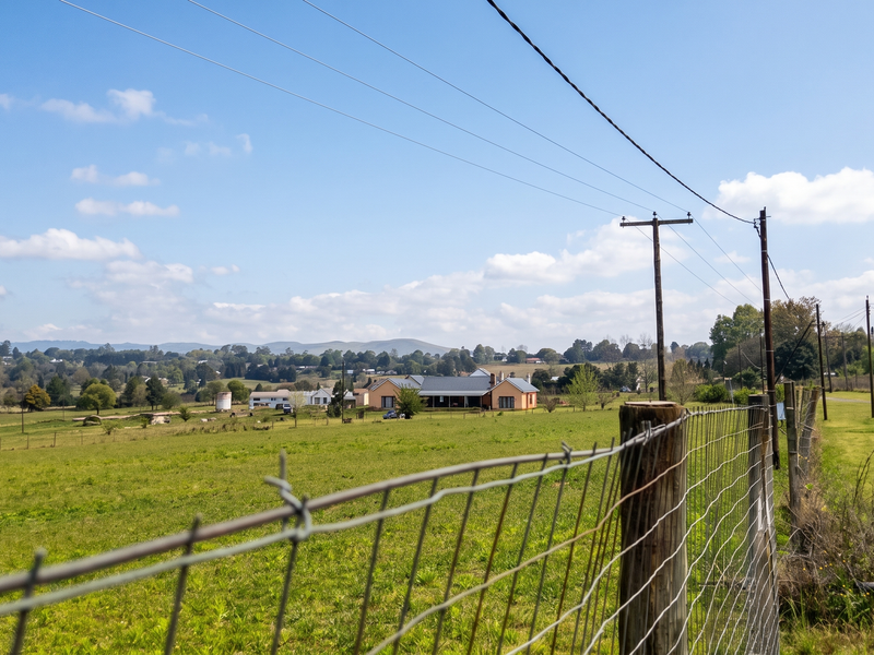 A scenic view of the surrounding rural landscape and open fields, featuring wire fencing and utility infrastructure in the foreground.