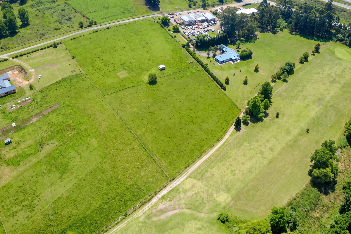 Aerial view of a large residential vacant land plot featuring open pasture, established fencing, and access roads, with neighboring properties visible.