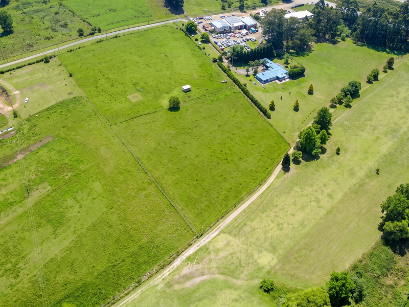 Aerial view of a large residential vacant land plot featuring open pasture, established fencing, and access roads, with neighboring properties visible.