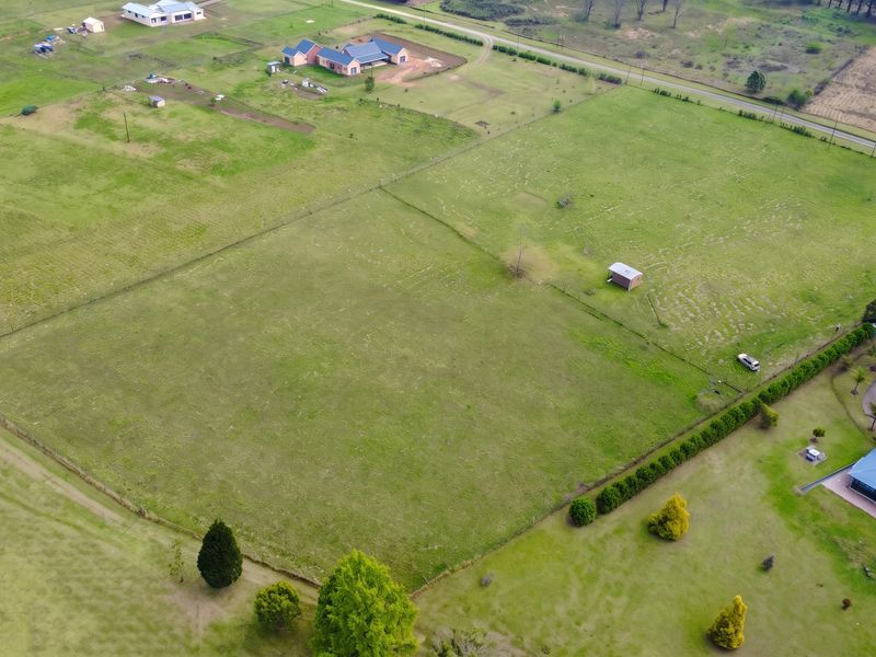 An aerial view of a large, open residential vacant land plot featuring perimeter fencing and a small storage shed.