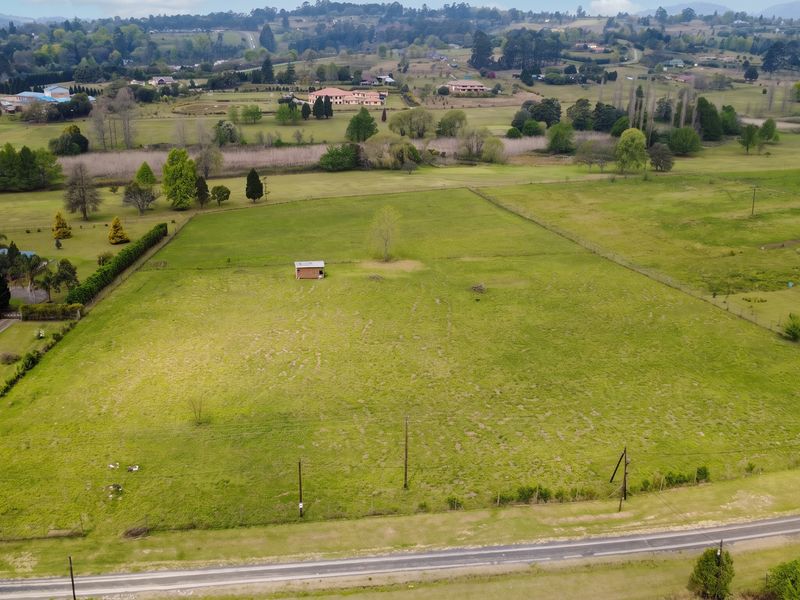 An aerial view of a large, open residential vacant land plot featuring perimeter fencing, a small shed, and surrounding rural landscape.