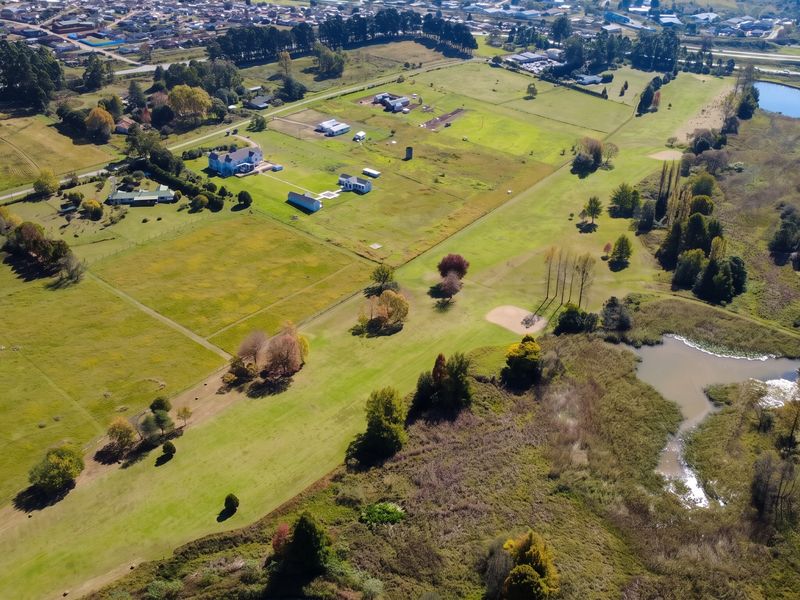 An aerial view of a large residential vacant land plot featuring open grassland, natural pond, and established trees in a rural setting.