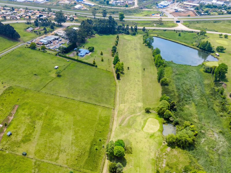 Aerial view of a large residential vacant land plot featuring open green space, a water dam, and proximity to a golf course fairway.