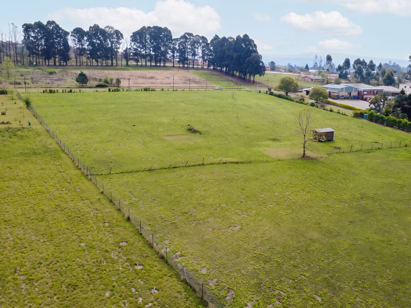 An aerial view of a large, open residential vacant land plot featuring perimeter wire fencing and a small storage shed.